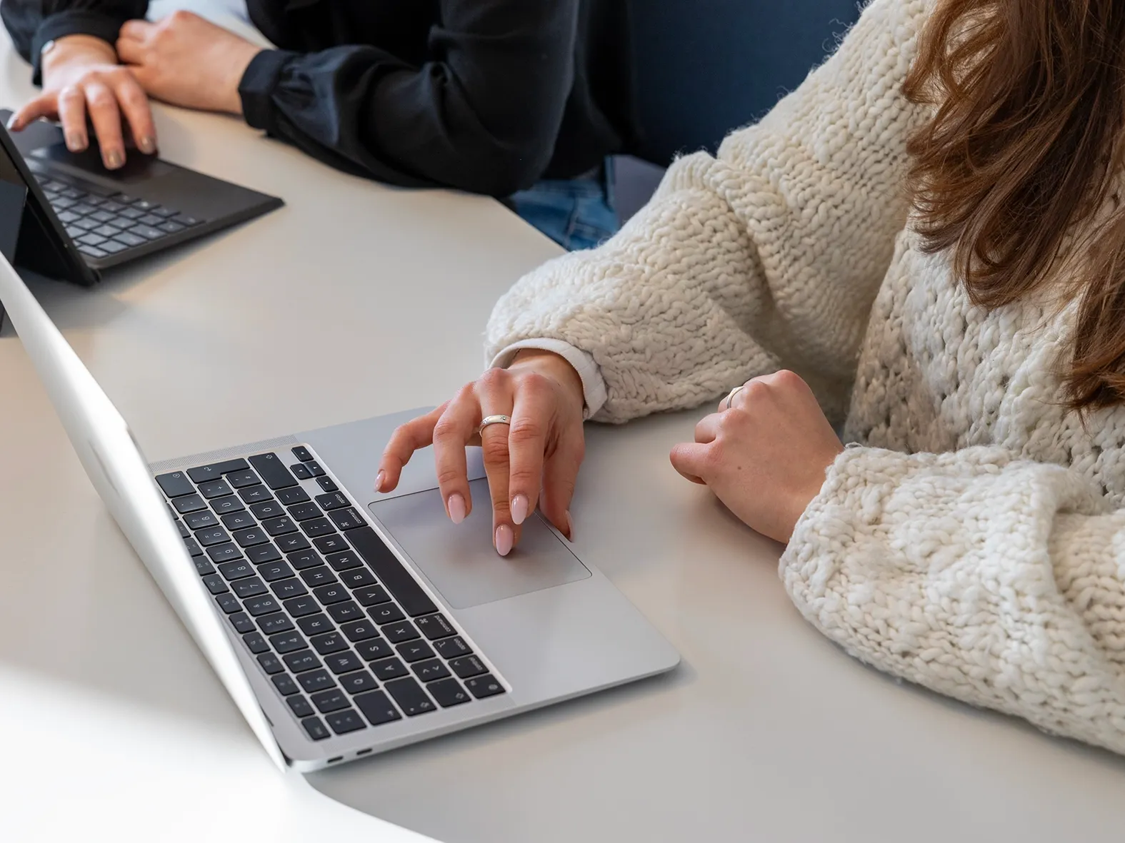 Nahaufnahme einer Person in heller Strickkleidung, die an einem Laptop arbeitet.