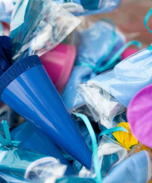 Mehrere bunte, in Folie verpackte Schultüten mit Bändern, Nahaufnahme in kräftigen Farben.