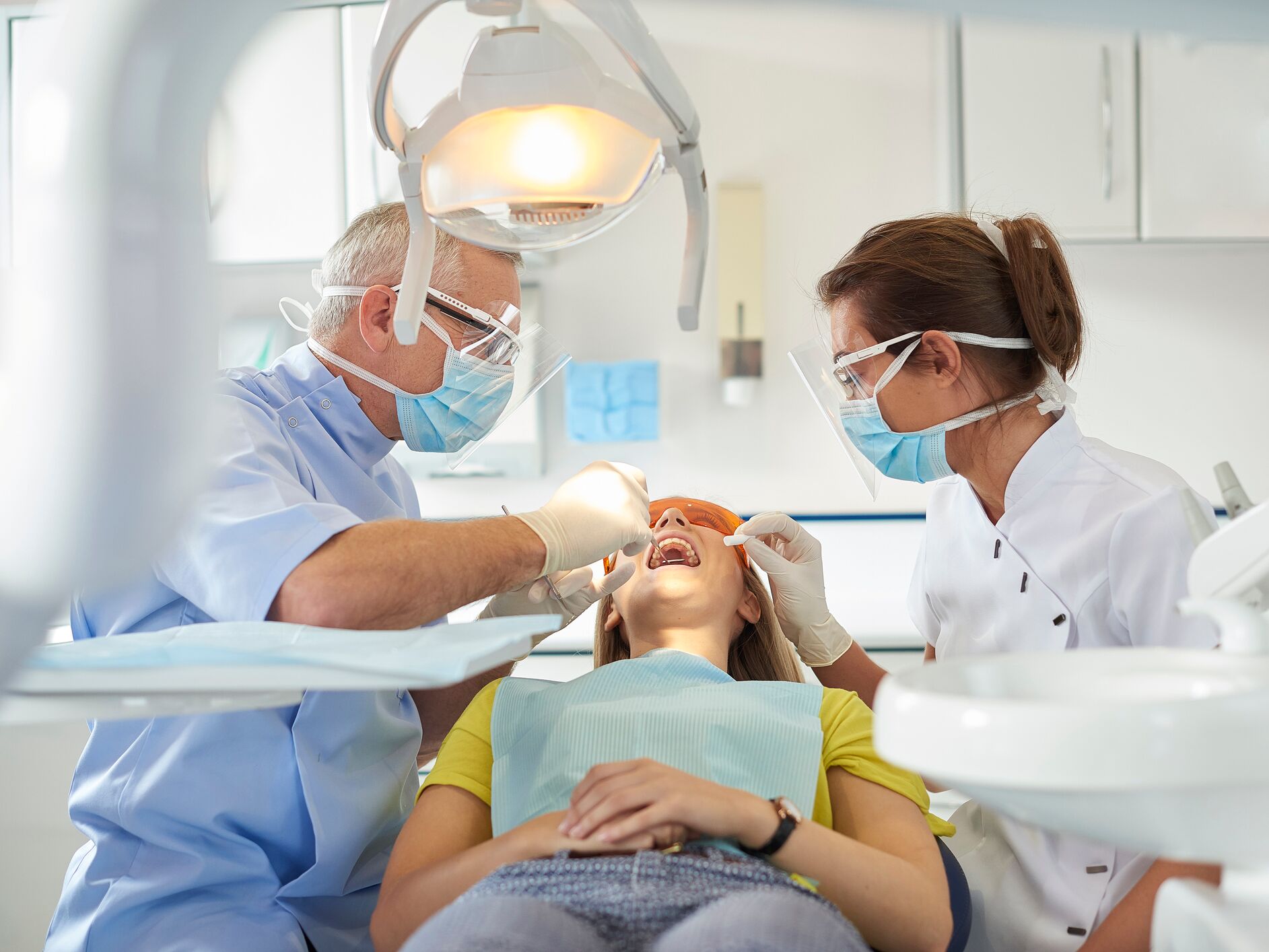 Zahnarzt und Assistentin behandeln eine Patientin auf dem Behandlungsstuhl unter einer hellen Lampe – Symbol für professionelle zahnärztliche Versorgung.