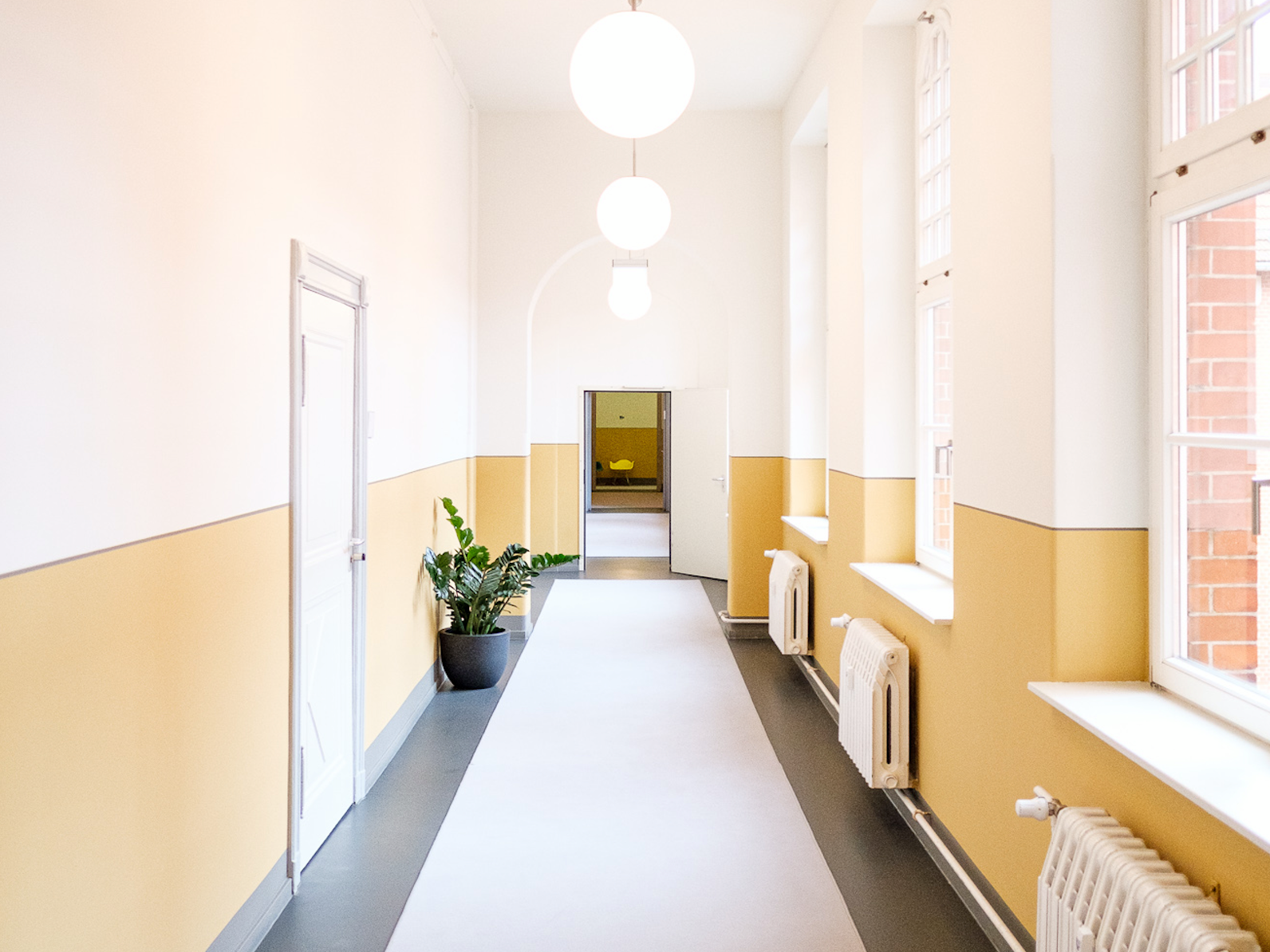 Heller Flur mit hohen Decken, gelb-weißen Wänden und einer Topfpflanze – freundliche und einladende Innenraumgestaltung.