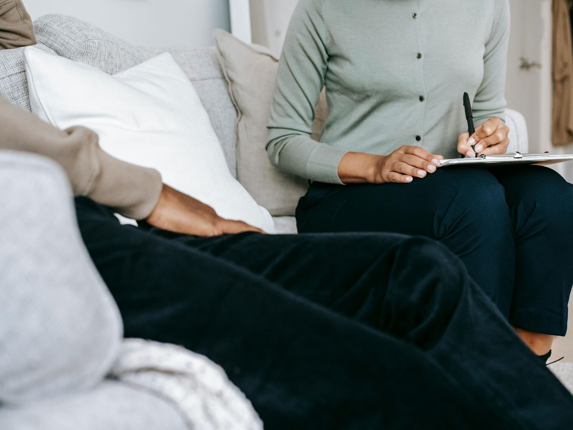 Zwei Personen sitzen auf einem Sofa, eine hält ein Tablet in der Hand, die andere sitzt entspannt gegenüber.