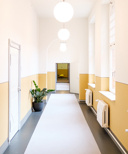 Heller Flur mit hohen Decken, gelb-weißen Wänden und einer Topfpflanze – freundliche und einladende Innenraumgestaltung.