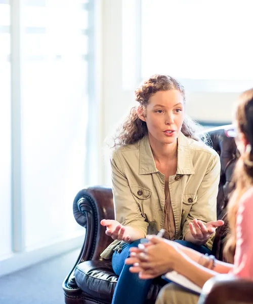 Zwei Personen sitzen einander gegenüber im Gespräch, eine davon hört aufmerksam zu und spricht in heller Umgebung.