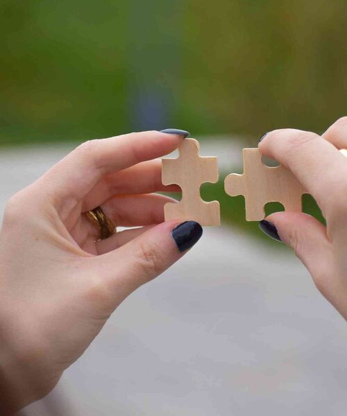 Zwei Hände halten passende Puzzleteile, die gleich ineinandergesteckt werden sollen.