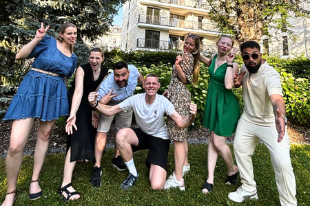 Gruppe junger Menschen posiert fröhlich und ausgelassen im Garten vor einem Gebäude.
