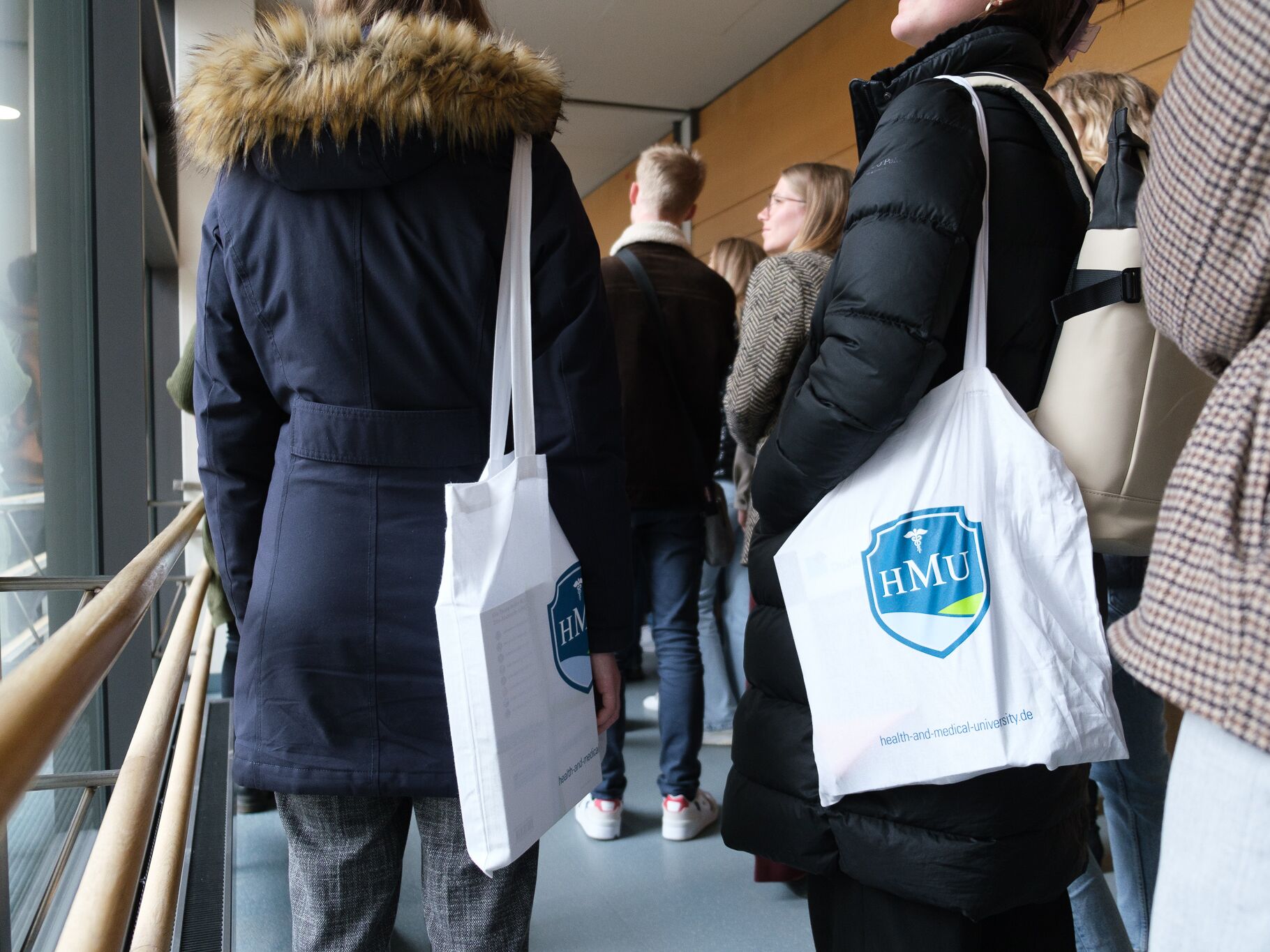 Mehrere Personen stehen zusammen, zwei tragen weiße Stofftaschen mit dem Logo der HMU – Health and Medical University.