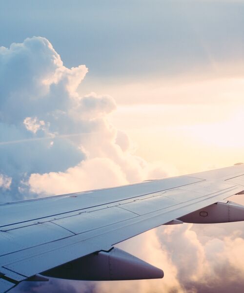 Blick aus dem Flugzeugfenster auf den Flügel über den Wolken bei Sonnenlicht, Symbol für Reisen und Aufbruch.