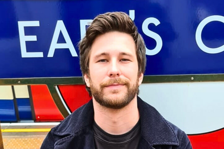 Person steht vor einem bunten Schild einer U-Bahn-Station und blickt ruhig in die Kamera.