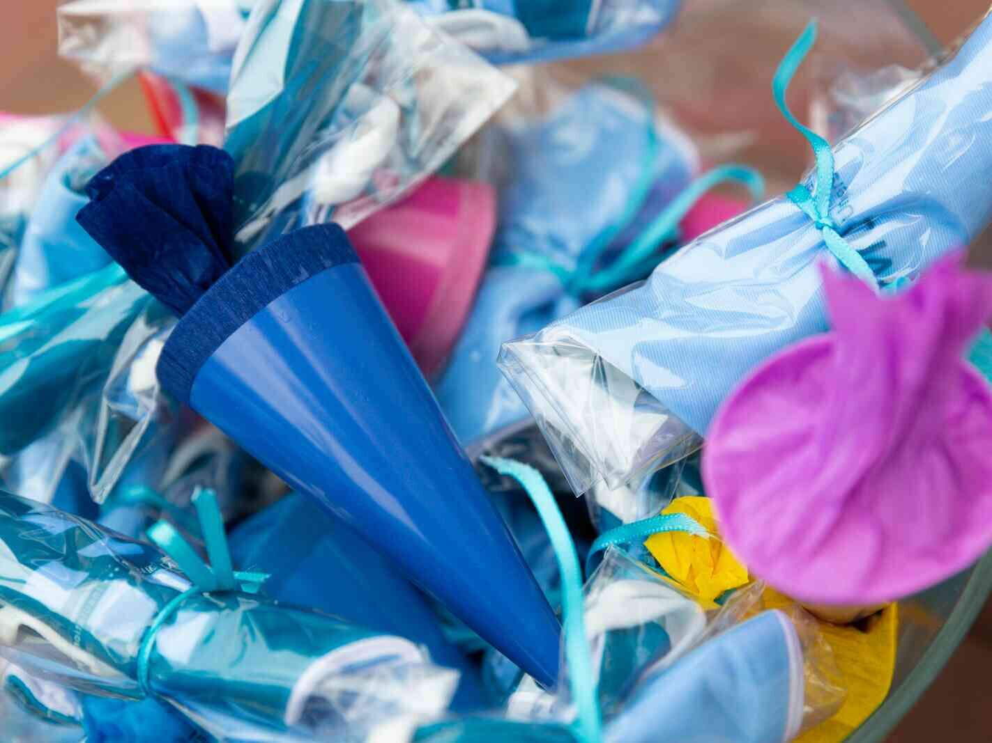 Mehrere bunte, in Folie verpackte Schultüten mit Bändern, Nahaufnahme in kräftigen Farben.