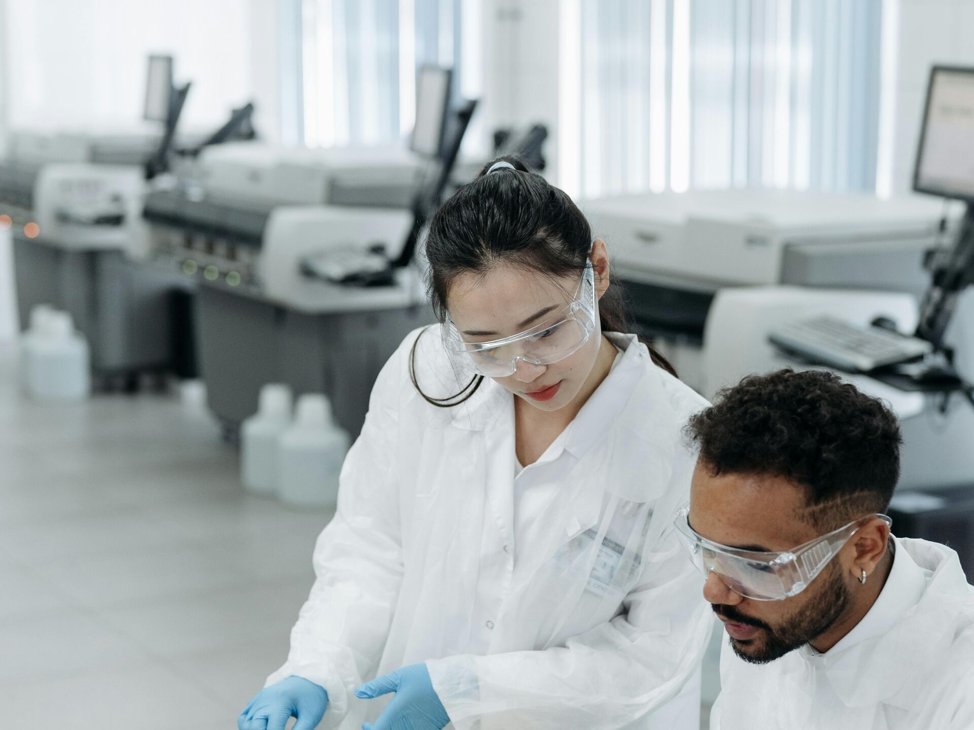 Zwei Personen in Laborkleidung und Schutzbrillen arbeiten gemeinsam an Unterlagen – Symbol für wissenschaftliche Zusammenarbeit und Forschung.